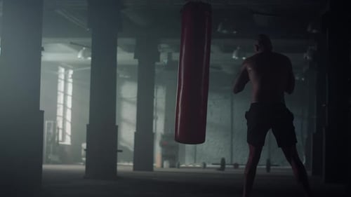 Man Boxing a Punching Bag in Dark Gym