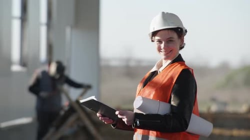 Female Engineer in Protective Helmet with Drawings in Hand on Background of Man with Welding Machine