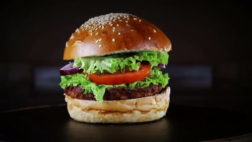 Burger with cutlet rotates on a wooden Board on a black background.