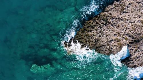 Flying up above Crystal Clear Water in the Sea. Waves Crashing against Rocks. Aerial top view