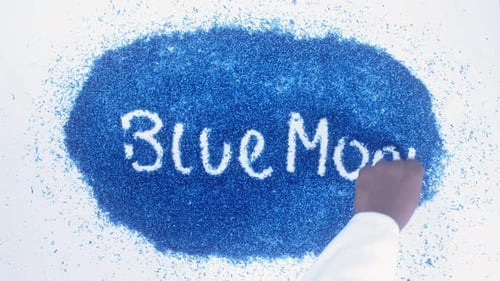 Hand Writes "Blue Moon" on Blue Shavings Pile