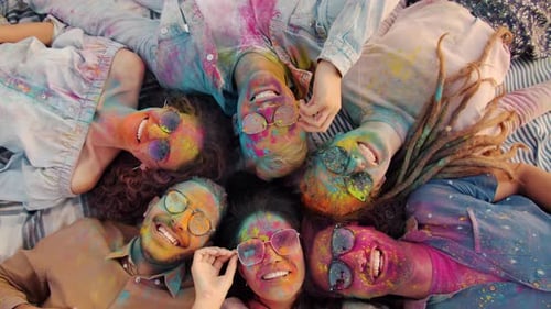 Top View of Happy Girls and Guys Lying on Grass with Painted Faces Enjoying Holi Festival
