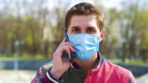 Junger Mann mit medizinischer Maske telefoniert im Park