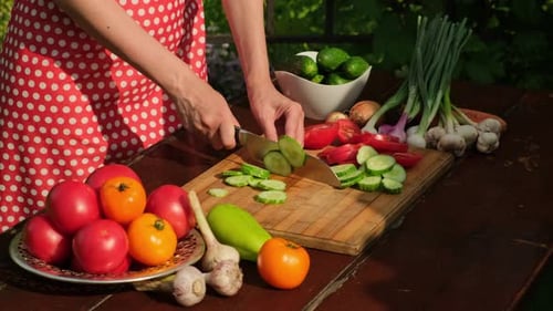 Woman cooking vegetable salad in kitchen. Woman's hands cutting with knife green cucumbers