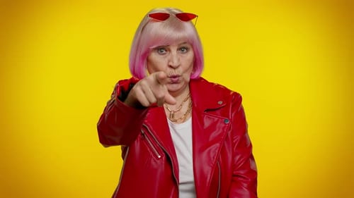 Ältere alte Frau zeigt mit verspieltem, fröhlichem Ausdruck auf die Kamera und zeigt die Richtung