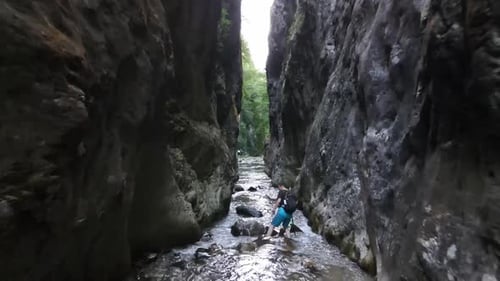 Man Hiking Through Rocky Stream in Narrow Canyon