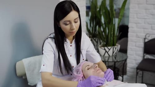 A beautician cleans the skin of the client's face before the procedure using a sponge