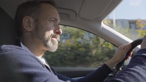 Ein gutaussehender kaukasischer Mann mittleren Alters schaut sich um, als er ein Auto durch ein Stadtgebiet fährt