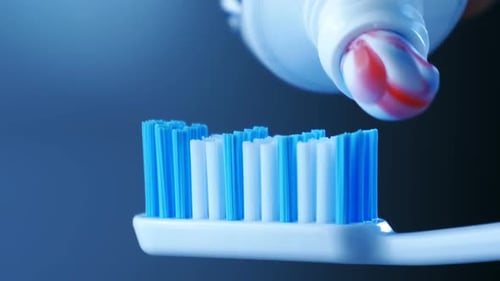 Zahngesundheit - Drücken Sie Zahnpasta mit bunten Streifen aus einer Tube auf eine Zahnbürste.