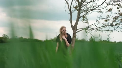 Blonde Woman Stands by Tree in Green Field