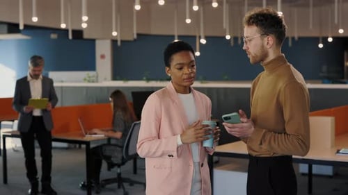Confident Office Worker Showing Something to His Female Coworker at the Smartphone