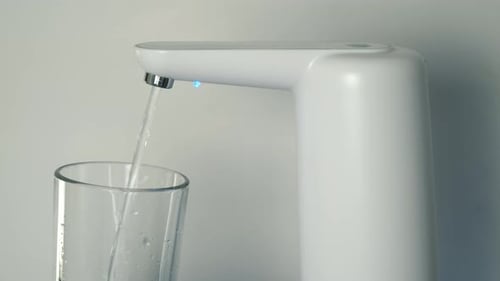 Clear Water is Pouring Into Glass From an Automatic Water Cooler Closeup View