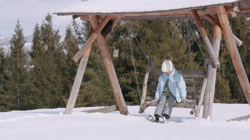 Girl Sits on Swing in Snowy Winter Landscape