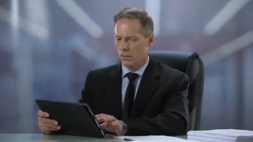 Selbstbewusster männlicher Chef arbeitet am Schreibtisch am Tablet-PC, Online-Dokumentation