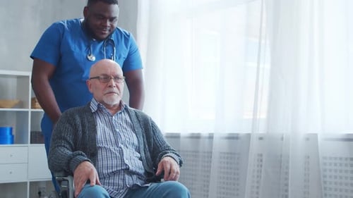 Nurse Helping Senior Man in Wheelchair Indoors