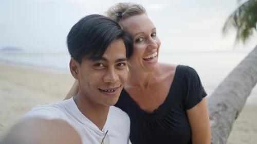 Happy Interracial Couple Dating on a Beach and Take a Selfie Video or Photo Kissing and Looking at