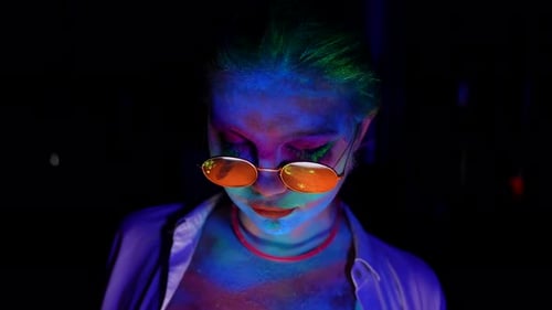 Portrait d'une femme folle et excentrique dans l'obscurité avec une lumière ultraviolette Le maquillage brille dans les flashs UV