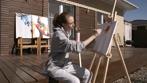 Woman Painting Artwork on Porch of Suburban House