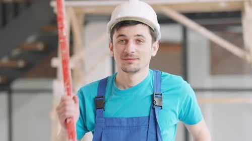 Smiling Construction Worker Carrying Level Indoors