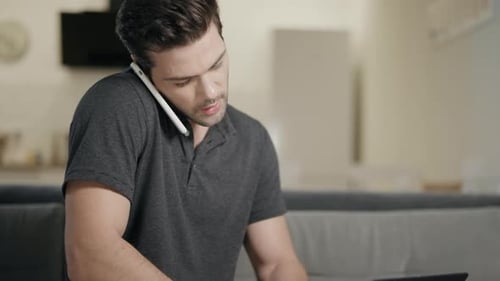 Man Works on Laptop at Home While on Phone