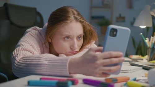 Auburn-haired Woman Looks at Phone at Desk