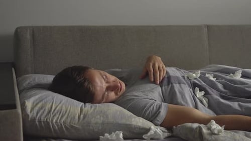 Man Resting in Bed Surrounded by Used Tissues