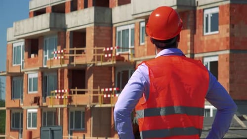 Construction Worker Looks Around and Thinks in Front of Building Site - Shot on Back