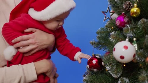 Baby Touches Christmas Ornament While Being Held Indoors