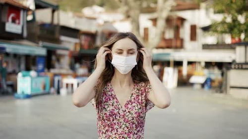 Woman Puts on Surgical Mask in Urban Setting