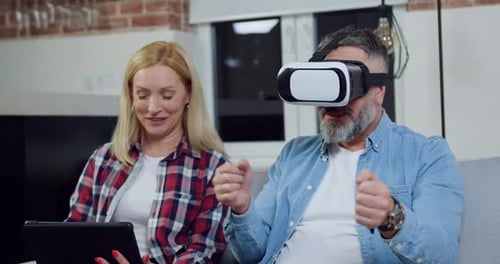 Mujer que usa una tableta mientras su esposo juega un juego de carreras en realidad virtual