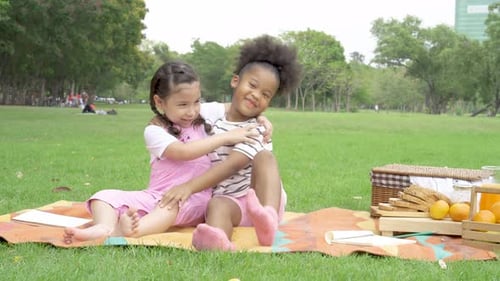 Two cheerful little girl sitting on the mat and hugging each other with love in the garden