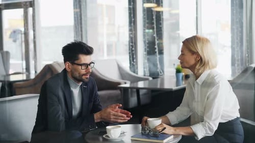 Businessman Talking To Attractive Mature Woman Coworker in Cafe at Table