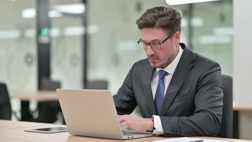 Focused Middle Aged Businessman Working on Laptop in Office