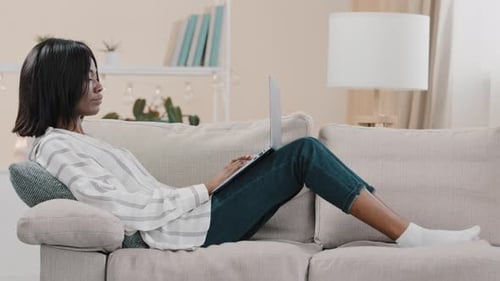 Woman Works on Laptop, Relaxing on Couch at Home