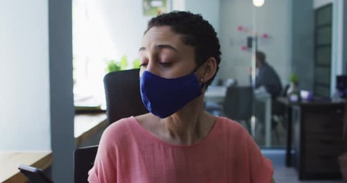 Caucasian woman wearing face mask sneezing on her elbow at modern office