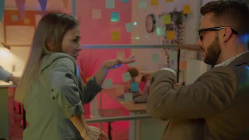 Câmera lenta de colegas de trabalho, homem e mulher, dançando e rindo, curtindo uma festa no escritório à noite