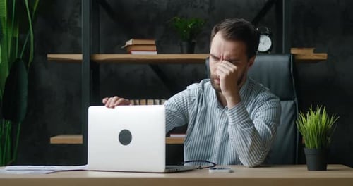 Bearded Man Massaging Temples at Office Desk