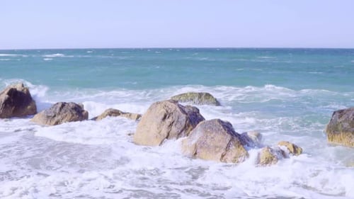 Les vagues de la mer se brisent sur un rocher formant une écume de mer par une journée ensoleillée