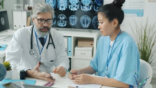 Nurse in Scrubs Looking at Tablet Screen and Talking to Doctor in White Coat in Modern Clinic