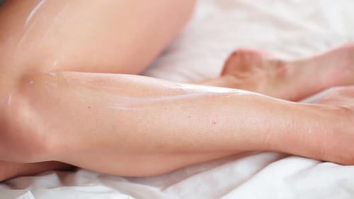 Woman Applies Lotion to Legs on Bed