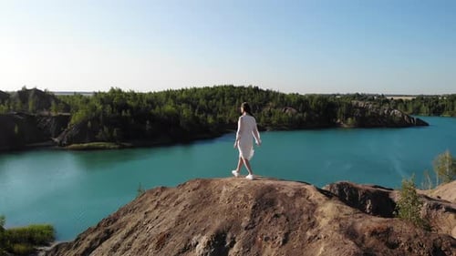 Schöne schlanke Frau in langem weißen Kleid nähert sich dem Rand des Abgrunds und breitet ihre Arme zur Seite