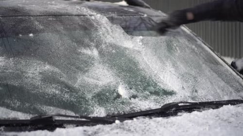 Ein Mann reinigt die Windschutzscheibe seines Autos mit einer Schaber-Nahaufnahme von Eis