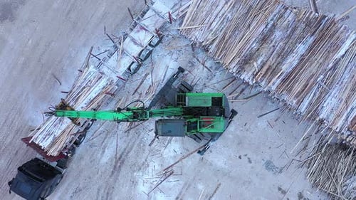 A Track Material Handler is Loading Logs Onto a Conveyor at the Factory
