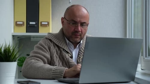 Serious Man with Glasses Opens the Laptop and Starts Typing on the Keyboard