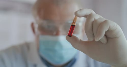 A Male Scientist Holds a Red Glass Ampoule with a Vaccine and Looks at It Close-up Slow Motion