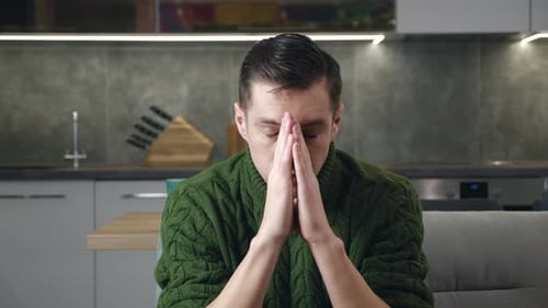 Worried Man With Hands Clasped Sits Indoors