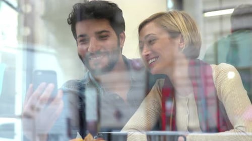Video call. Happy couple using phone in cafe indoors
