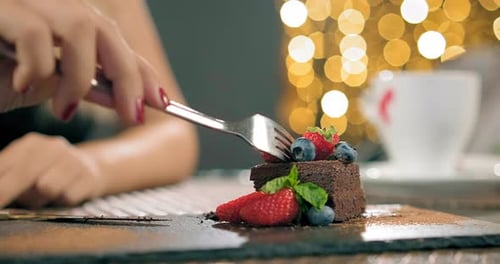 Woman Eating Chocolate Cake with Berries at Night