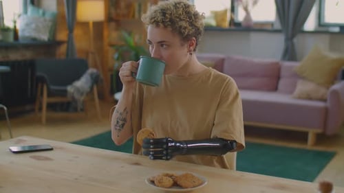 Girl with Prosthetic Arm Drinking Tea with Cookie at Home