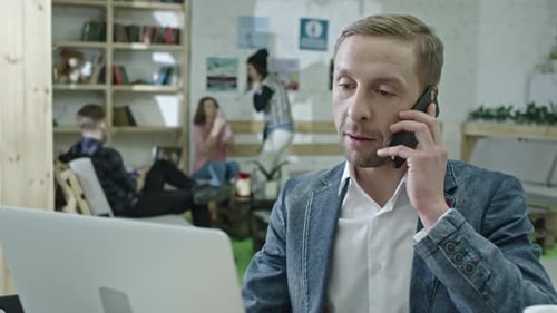 Man Working at Laptop Answers Mobile Phone